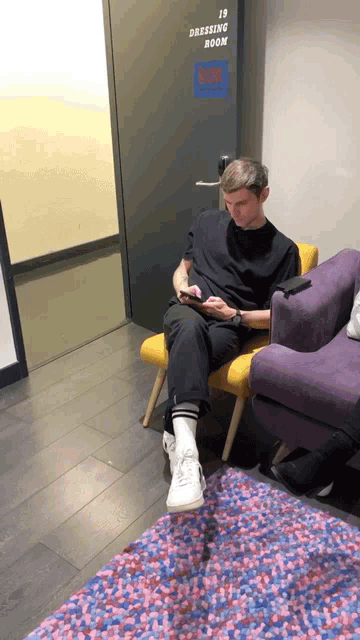a man sits on a chair in front of a door that says dressing room