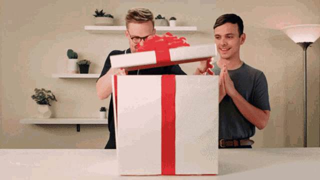 two men open a gift box with a red ribbon