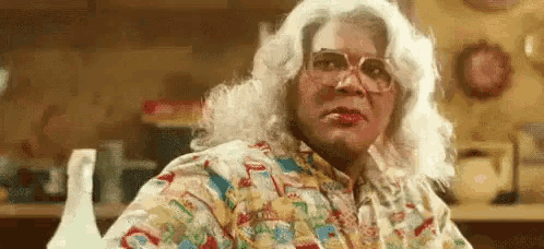 a woman wearing glasses and a wig is sitting at a table .