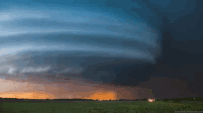 a storm is coming in over a field with a house in the foreground