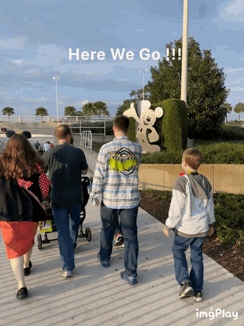 a group of people walking in front of a mickey mouse statue with the caption here we go !!!