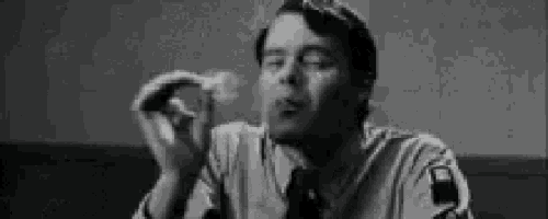 a man in a suit and tie is smoking a cigarette .