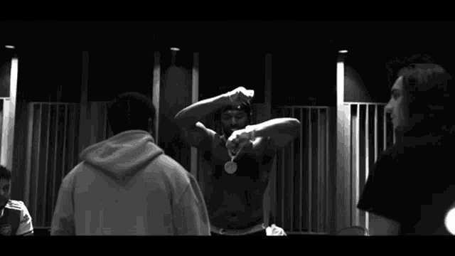 a black and white photo of two men standing next to each other . one of the men is wearing a hoodie .