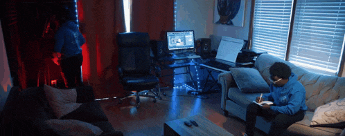 a man in a blue sweatshirt sits on a couch in front of a keyboard