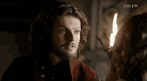 a man with long hair and a beard is standing next to a woman in a room with a candle .
