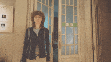 a woman stands in front of a door that has a green sign on it that says salida
