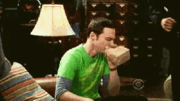 a man wearing a green shirt is sitting on a couch and blowing his nose