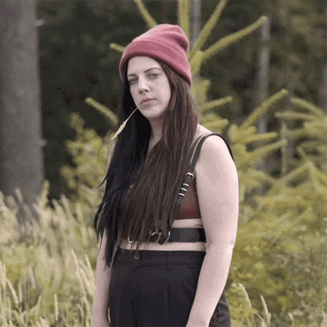 a woman wearing a red beanie and a crop top stands in a field