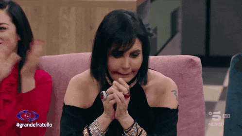 a woman sitting on a pink couch with the words grandefratello on the bottom of the screen