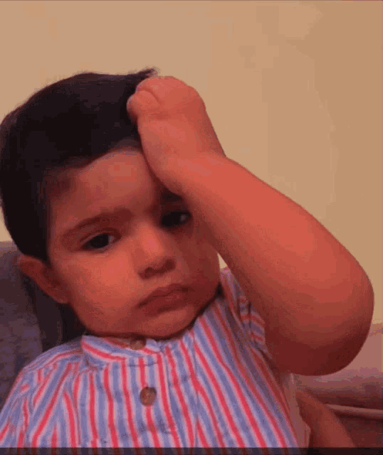 a little boy in a striped shirt holds his hand to his forehead