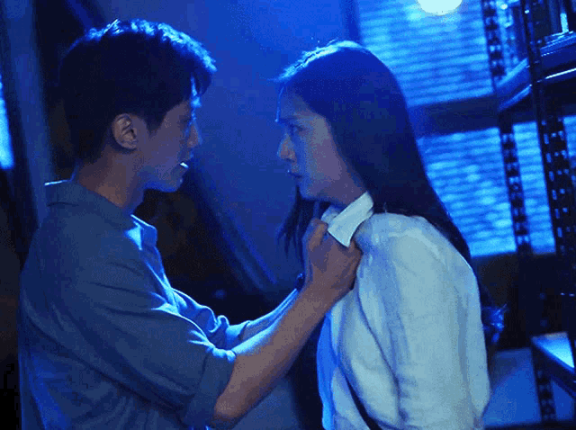 a man adjusts a woman 's shirt collar in a dark room
