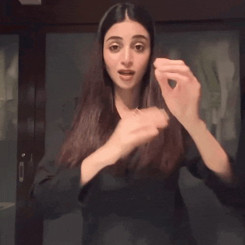 a woman in a black jacket holds her hands up