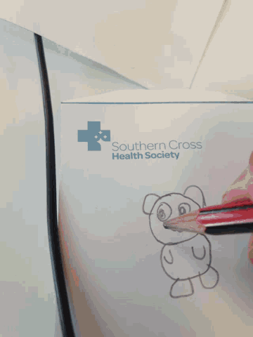 a person is drawing a teddy bear with a pencil on a piece of paper that says southern cross health society