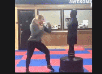 a woman is kicking a punching bag in a gym with a sign that says awesome