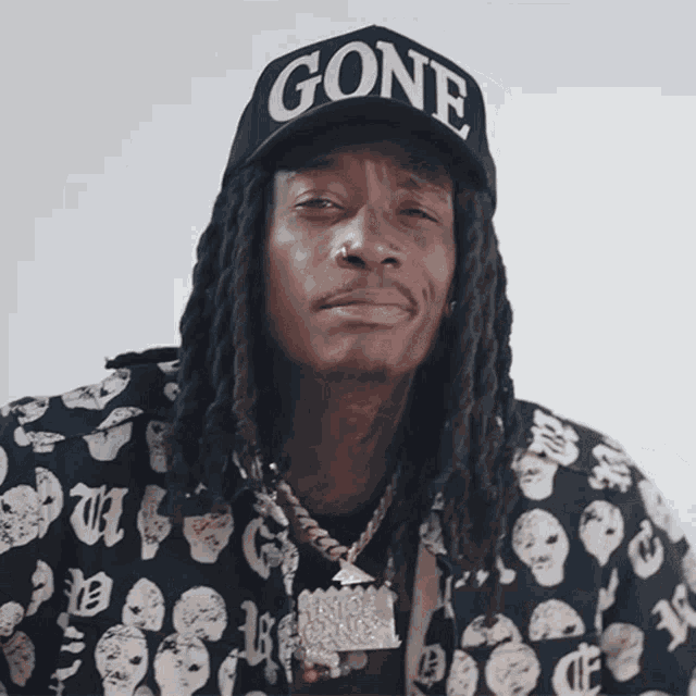 a man with dreadlocks wears a black hat that says gone