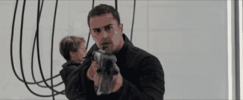 a man in a black jacket is holding a gun in front of a wall .