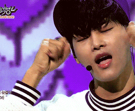a man wearing a hat and a striped shirt is singing into a microphone on a stage with a purple background