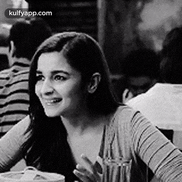 a black and white photo of a woman sitting at a table in a restaurant .