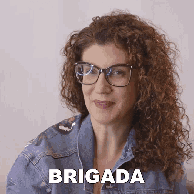 a woman with curly hair wearing glasses and a denim jacket says " brigada "