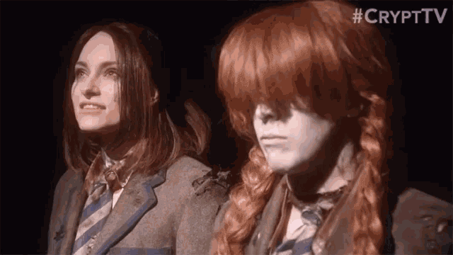 two girls with red hair are standing next to each other in a dark room . one of the girls is wearing a wig .