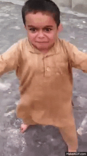 a young boy in a brown shirt and pants is standing on the ground with his arms outstretched .