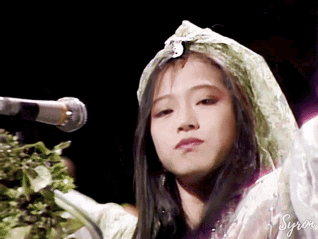 a woman is standing in front of a microphone wearing a veil and looking at the camera .