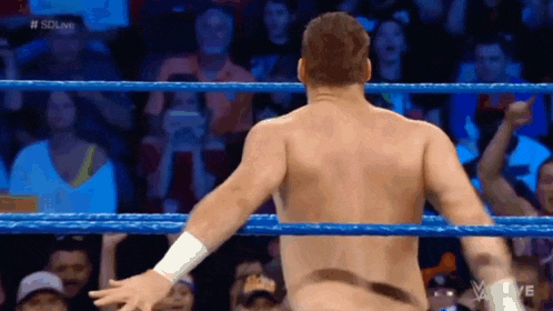 a man without a shirt is standing in a wrestling ring with his arms outstretched .