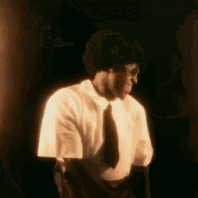 a man in a white shirt and tie is standing in the dark .