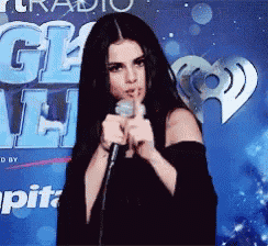 a woman is holding a microphone in front of a sign that says iheartradio