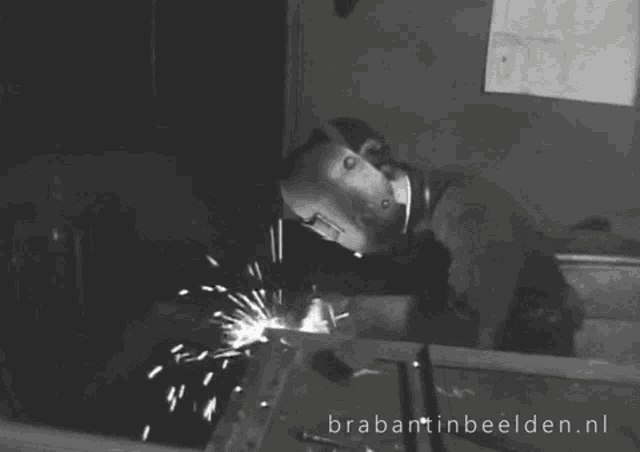a black and white photo of a man welding with the website brabantnbeelden.nl visible in the corner