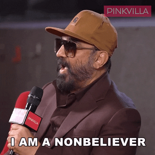 a man wearing a hat and sunglasses is holding a microphone and saying i am a nonbeliever