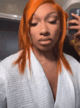 a woman with red hair is taking a selfie with her phone while wearing a white robe .