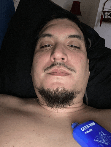 a man with a beard is laying in bed with a geek bar pulse on his chest