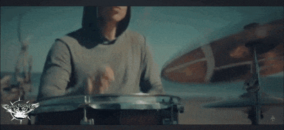 a man in a hooded shirt is playing drums on a beach
