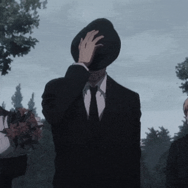 a man in a suit and tie covers his face with his hat