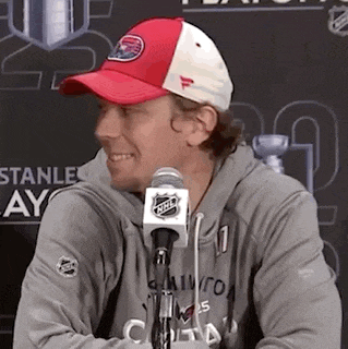 a man wearing a red and white hat and a gray hoodie is sitting in front of a microphone .