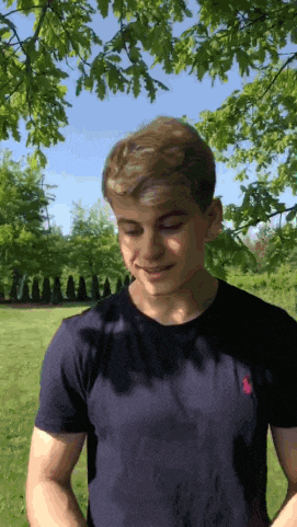a young man wearing a black polo shirt is standing in a park