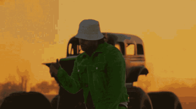 a man wearing a green jacket and a white hat stands in front of a truck