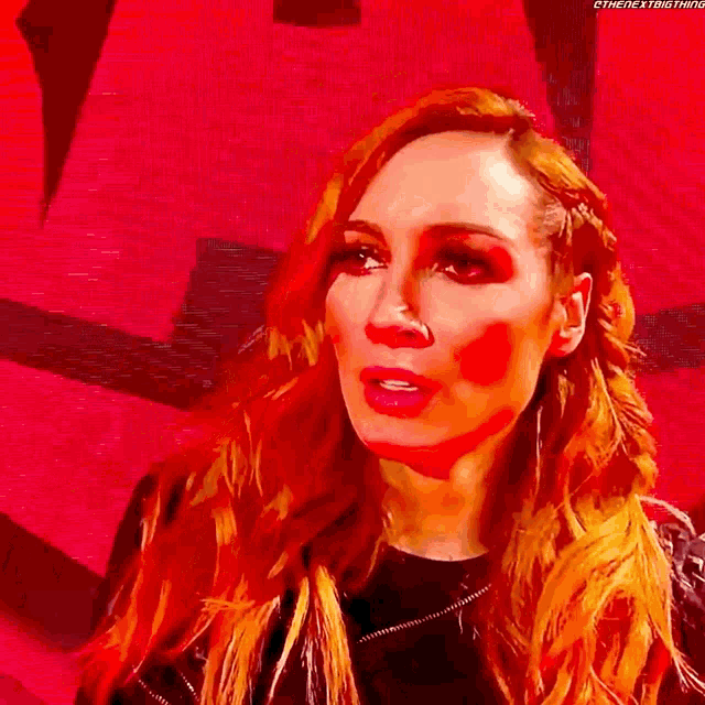 a woman with long red hair is standing in front of a red background and looking at the camera .