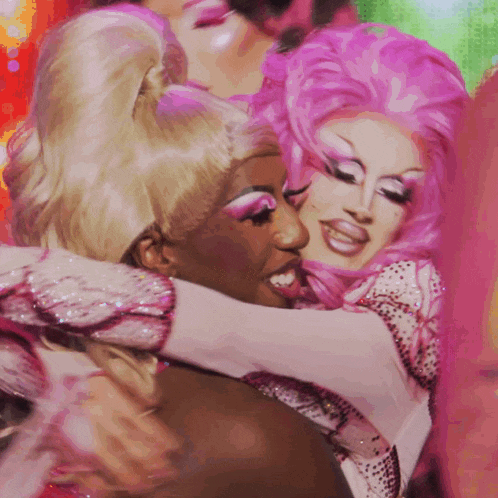 two drag queens are hugging each other and one is wearing a pink wig