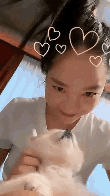 a woman is petting a small white dog with hearts drawn on her head .