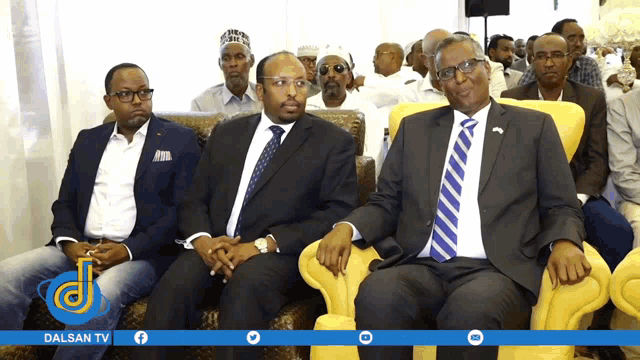 a group of men are sitting in front of a dalsan tv ad