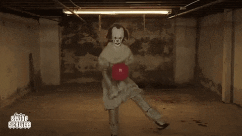 pennywise the clown is holding a red ball in a basement .