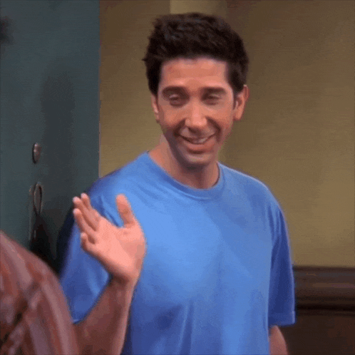 a man in a blue shirt is smiling and making a peace sign