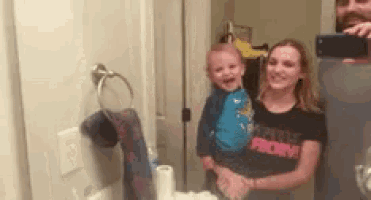 a woman is holding a child in front of a mirror while wearing a shirt that says priority