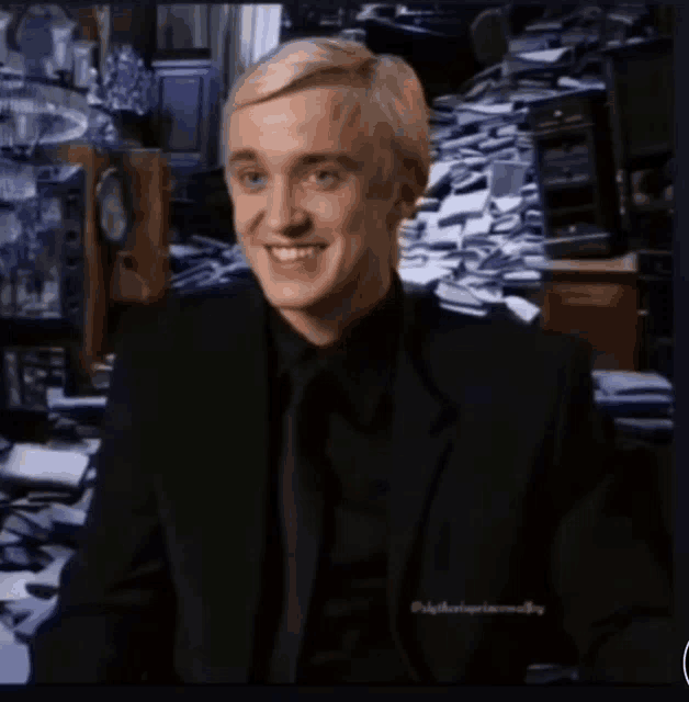 a man in a black suit and tie is smiling in front of a pile of papers