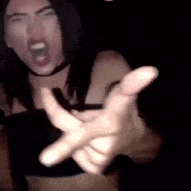a woman in a black top is screaming and making a funny face while holding out her hand .