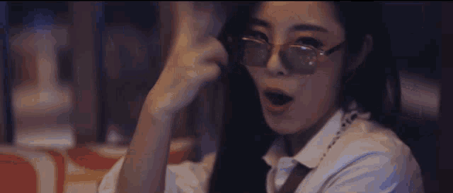 a woman wearing sunglasses and a white shirt is sitting in a dark room
