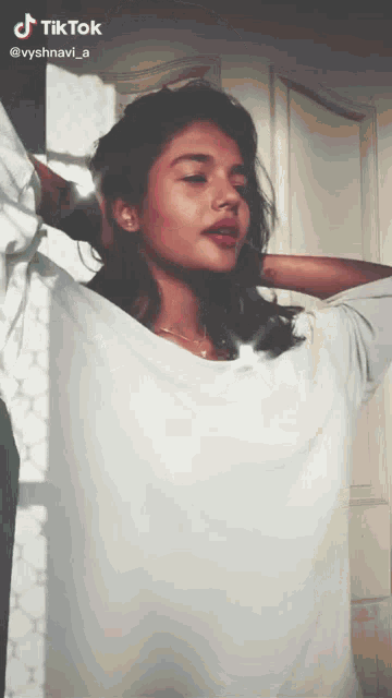 a woman in a white shirt is standing in front of a window with tiktok written on the bottom