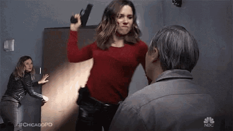 a woman is pointing a gun at a man in a room while two other women look on .